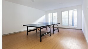 Une pièce avec une table de ping-pong, de grandes fenêtres et un plancher en bois.