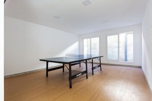 Habitación con mesa de ping pong, ventanas amplias y suelo de madera.