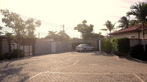 Une allée pavée mène à une entrée fermée par un portail, où une voiture est garée.