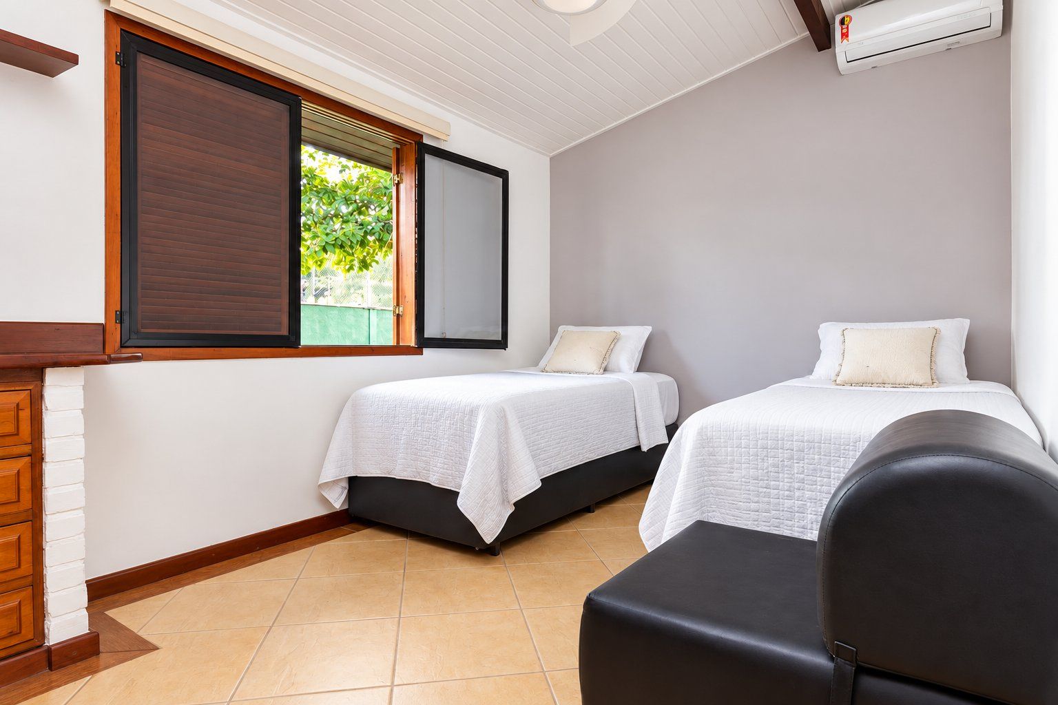 A bedroom with two beds, a window with a view, a white wall, and a ceiling fan.