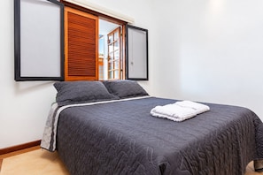 Uma cama de solteiro com um edredom acolchoado escuro, duas almofadas e uma toalha branca dobrada na cama.