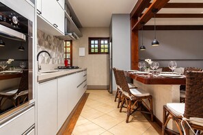 Cozinha moderna com armários brancos, forno embutido e área de jantar com cadeiras de vime e mesa de madeira.