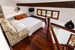 A bedroom with a bed, a wooden dresser, a television, and a window with a view.