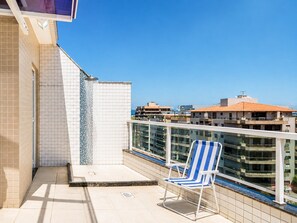 Un balcón con suelo de baldosas, balaustrada de cristal y una silla lounge azul y blanca.
