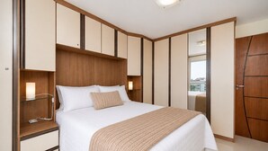 Ein modernes Hotelzimmer mit einem großen Bett, integrierten Regalen, einem Nachttisch und einem Kleiderschrank.