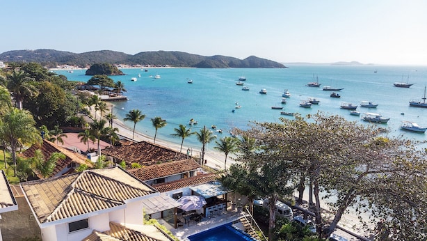 A coastal hotel with a beach view, multiple boats in the water, and palm trees.