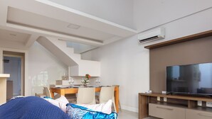 A modern hotel room with a dining area, a large flat-screen TV, and an air conditioning unit.