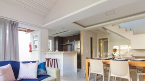 A modern living room with a sofa, a dining table set for four, and a kitchen in the background.