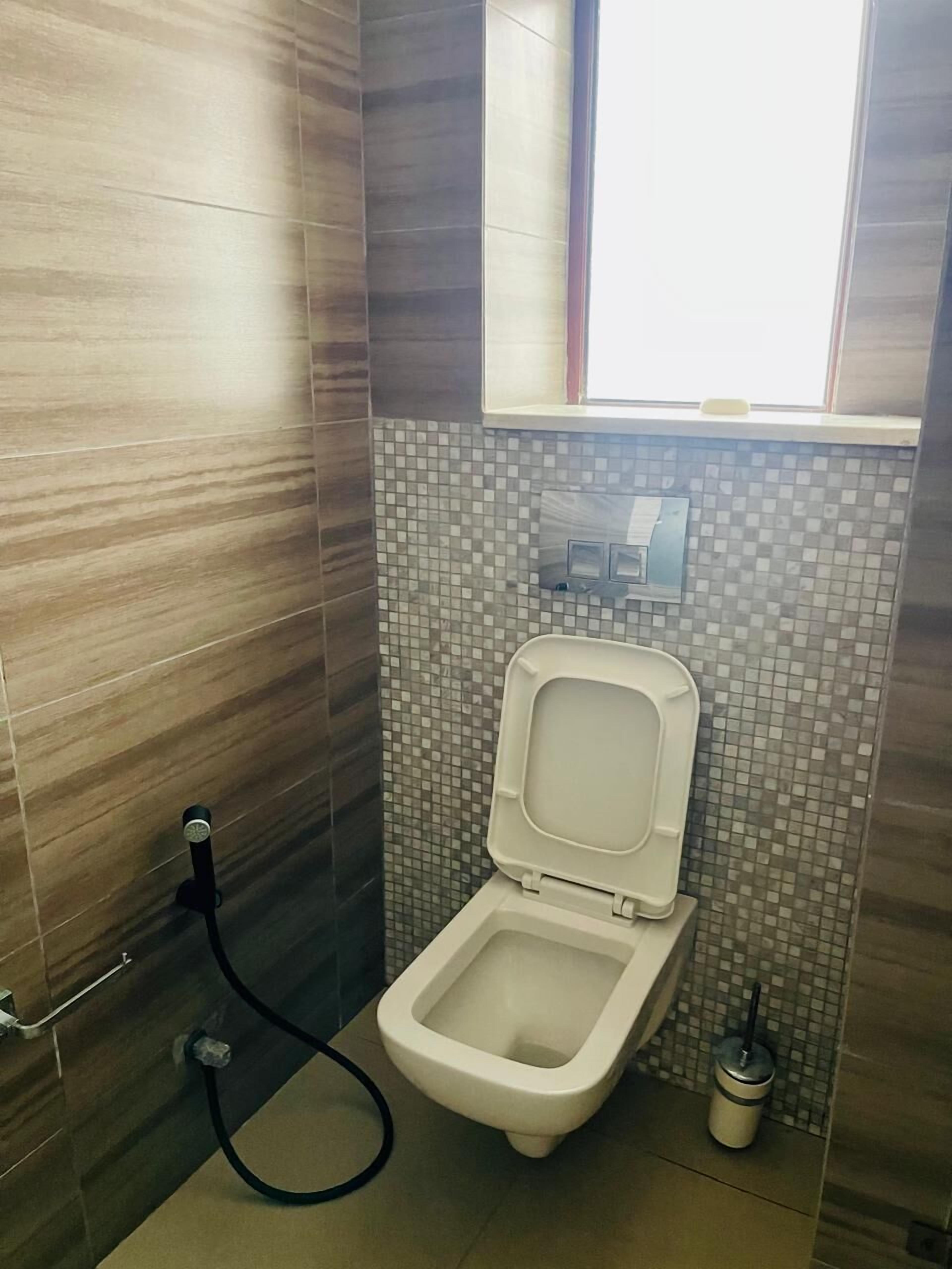 A small bathroom with a toilet, a window, and a tiled backsplash.