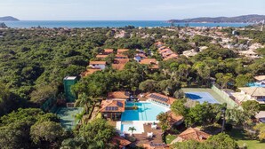 An aerial view of a resort with a swimming pool, surrounded by lush greenery and a coastal backdrop. - BZ03 House in a Club Condominium Steps from the Beach (Armação dos Búzios)