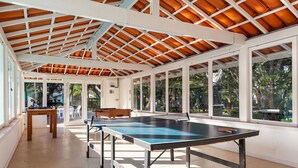 A spacious indoor area with a ping pong table, large windows, and a wooden ceiling structure. - BZ03 House in a Club Condominium Steps from the Beach (Armação dos Búzios)