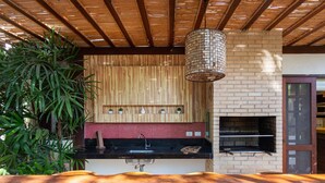 A kitchen with a brick oven, wooden ceiling beams, and a hanging light fixture. - BZ03 House in a Club Condominium Steps from the Beach (Armação dos Búzios)