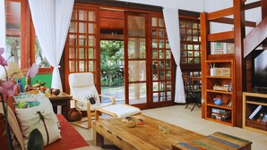 A room with a wooden coffee table, a white armchair, a bookshelf, and a television. - Bz10 House in a gated club community steps from the beach (Armação dos Búzios)