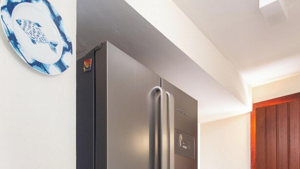 A stainless steel refrigerator in a kitchen with a wooden door and a blue and white wall decoration.