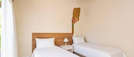 Una habitación con dos camas, un cabecero de madera, una mesita de noche con una lámpara y un tapiz de colores.