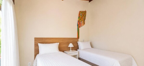 Una stanza con due letti, una testiera in legno, un comodino con una lampada e un arazzo colorato.