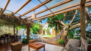 A covered outdoor area with a pool, wooden furniture, and a hammock.