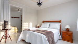 Un dormitorio ordenado con cama, mesitas de noche, televisor y ventilador de techo.