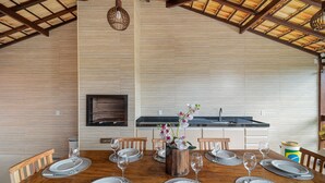 A dining area with a wooden table set for six, a kitchen in the background, and a wooden ceiling.