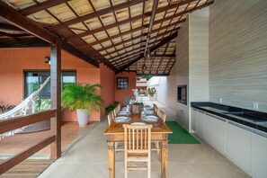 Un comedor cubierto con una mesa de madera dispuesta para seis personas, rodeado de plantas en macetas y una hamaca.