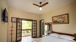 A hotel room with a bed, a ceiling fan, a TV, and a painting on the wall.