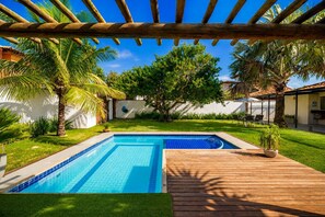 A swimming pool with a wooden deck, surrounded by palm trees and a white wall. - Bz04 30 steps from the beach! Beautiful house with a pool! (Armação dos Búzios)