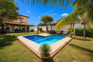 A swimming pool with a tiled deck, surrounded by grass and palm trees. - Bz04 30 steps from the beach! Beautiful house with a pool! (Armação dos Búzios)