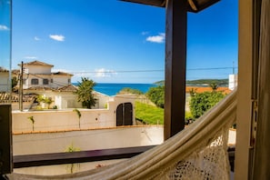 A balcony with a view of the sea, a white building with a tiled roof, and a hammock.