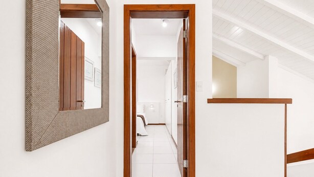 A hallway with a wooden door frame, a mirror, and a white tiled floor.