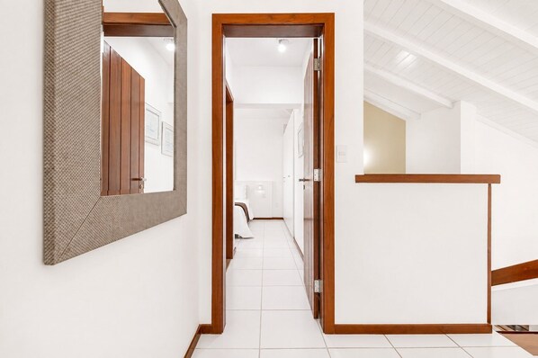 Un pasillo con un marco de puerta de madera, un espejo y un suelo de baldosas blancas.