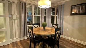A dining area with a round wooden table, black chairs, a central potted plant, and a hanging light fixture.