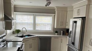 A modern kitchen with light-colored cabinets, stainless steel appliances, and a dark wood floor.