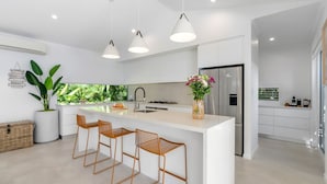 A modern kitchen with a central island, bar stools, a refrigerator, and a potted plant.