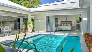 A modern house with a swimming pool, glass doors leading to a bedroom, and a patio area with outdoor furniture.