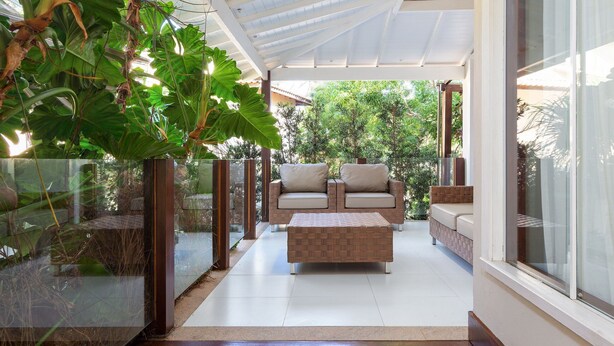 An indoor patio with a glass enclosure, a cushioned sofa, and a woven ottoman. - Bz05 House with pool and 5 Geribá suites! (Armação dos Búzios)