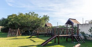 Un terrain de jeux doté de structures en bois, notamment d’un toboggan et d’échelles d’escalade, entouré de pelouse et d’arbres.