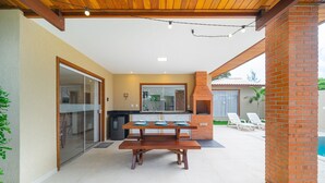An outdoor patio with a wooden table and benches, a brick chimney, and a pool in the background. - Bz38 House 150m from the beach with private pool (Armação dos Búzios)