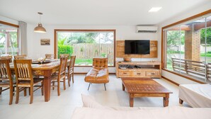 A spacious living room with a dining area, a leather sofa, a wooden coffee table, and a television on a wooden stand. - Bz38 House 150m from the beach with private pool (Armação dos Búzios)