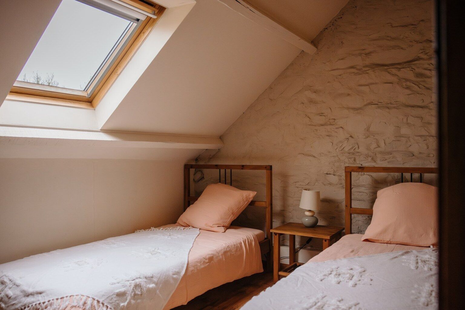 A small, cozy bedroom with two single beds, a skylight, and a stone wall.