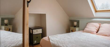 A bedroom with two beds, a skylight, and a small storage unit.