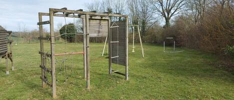 A wooden play structure in a grassy yard with a swing set and a climbing frame.