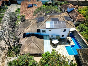 Ein Wohngebäude mit Ziegeldach, Solaranlage, Schwimmbad und umliegender Bepflanzung.