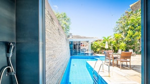 Une piscine avec un mur en verre, un espace extérieur aménagé pour s’asseoir et un mur en briques.
