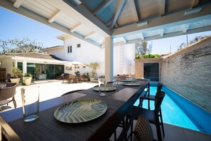 Ein Essbereich am Pool mit Tischen für zwei Personen, umgeben von Stühlen und freiem Blick auf den Pool.