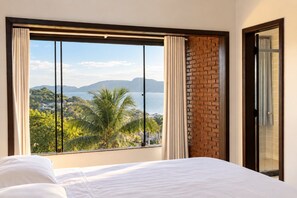 Ein Hotelzimmer mit großem Fenster und Blick auf eine Küstenlandschaft, einem Bett und einer Ziegelwand.