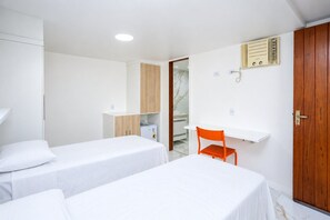 A hotel room with two single beds, a wooden wardrobe, a small table with a chair, and a built-in heater.