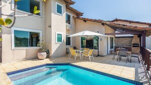 Una piscina con bordes de azulejos, un patio con mobiliario exterior y una chimenea de ladrillo.