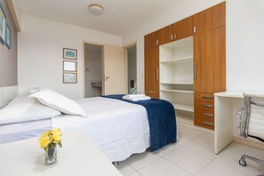 A hotel room with a bed, a desk, a chair, a wardrobe, and a bathroom visible through an open door.