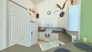 A compact kitchen with white cabinets, a refrigerator, an oven, and a microwave.