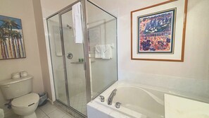 A bathroom with a glass-enclosed shower, a toilet, a bathtub, and a framed picture on the wall.